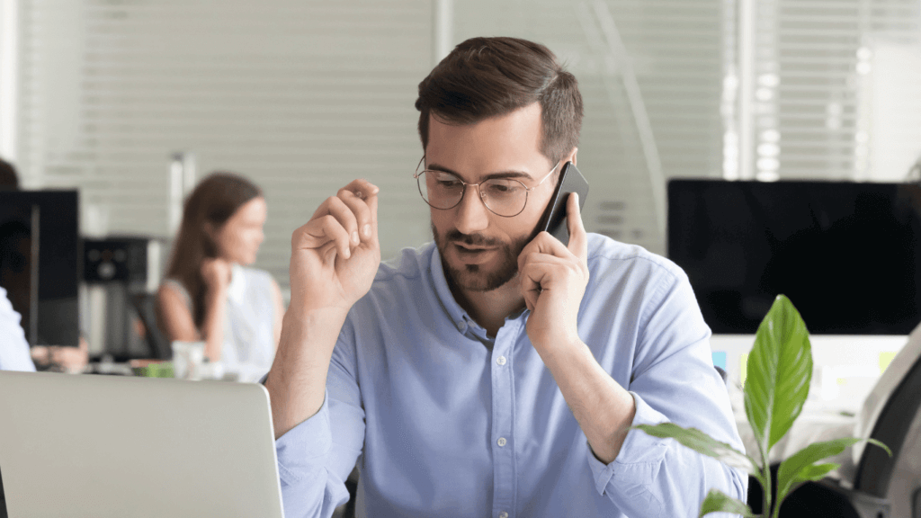 A sales person using a laptop to send a cold sales email while also talking on the phone to conduct initial outreach